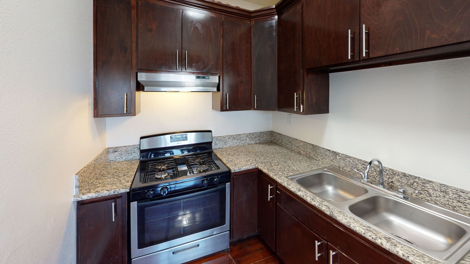 Kitchen with dark brown cabinets, granite countertops, stainless steel stove, and double sink.