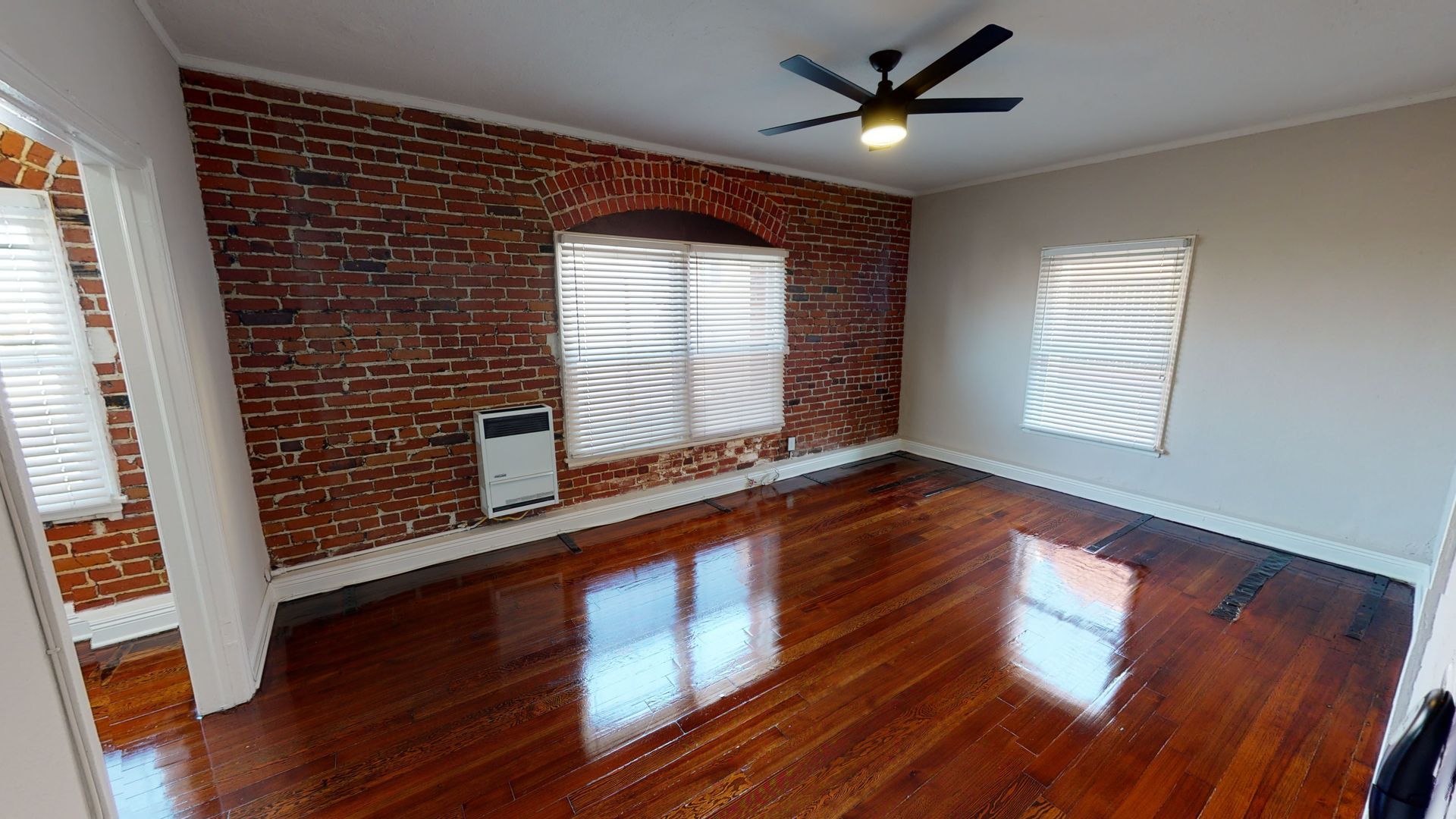Room with brick wall, hardwood floors, and windows; ceiling fan.