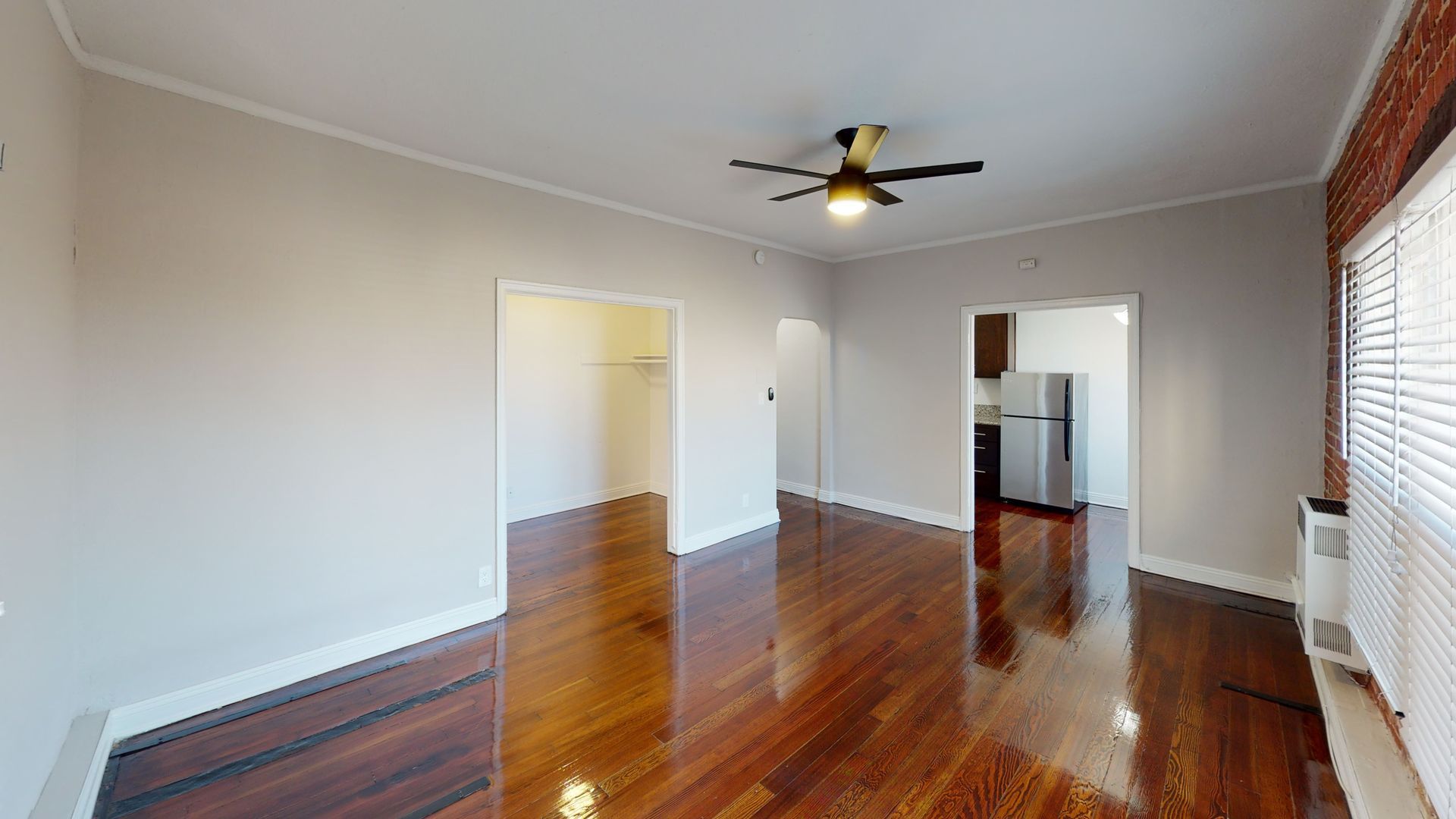 Spacious living room with wood floors, doorways, ceiling fan, and access to kitchen.