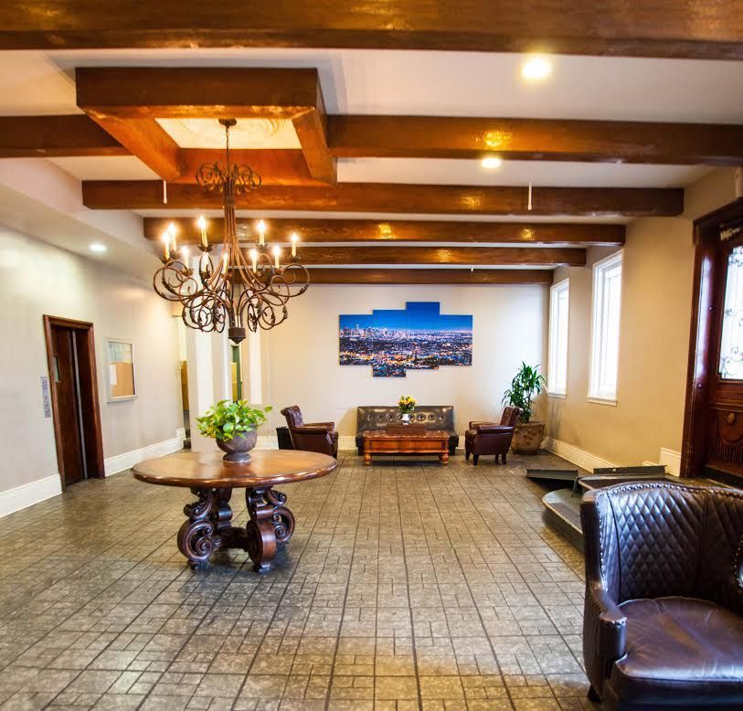 Lobby with ornate chandelier, wood beams, seating, and a cityscape photo.
