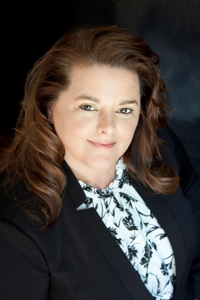A woman is sitting at a desk with a laptop and a vase of flowers.