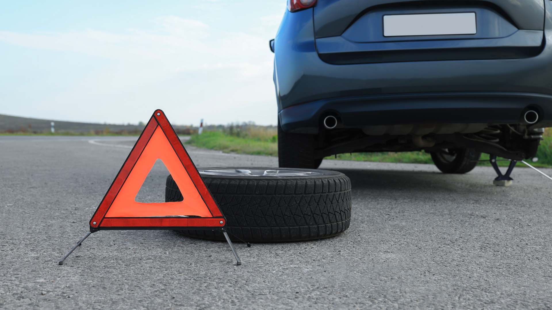 A car with a flat tire and a warning triangle on the side of the road.