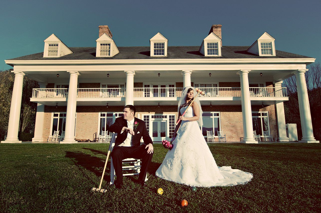 A bride and groom are playing croquet in front of a large house.