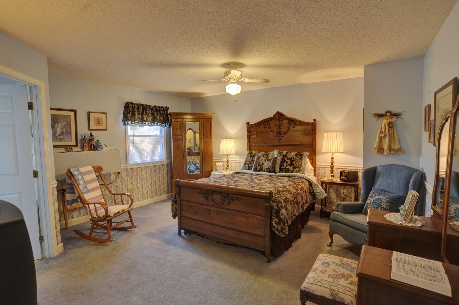 A bedroom with a king size bed , rocking chair , dresser and mirror.