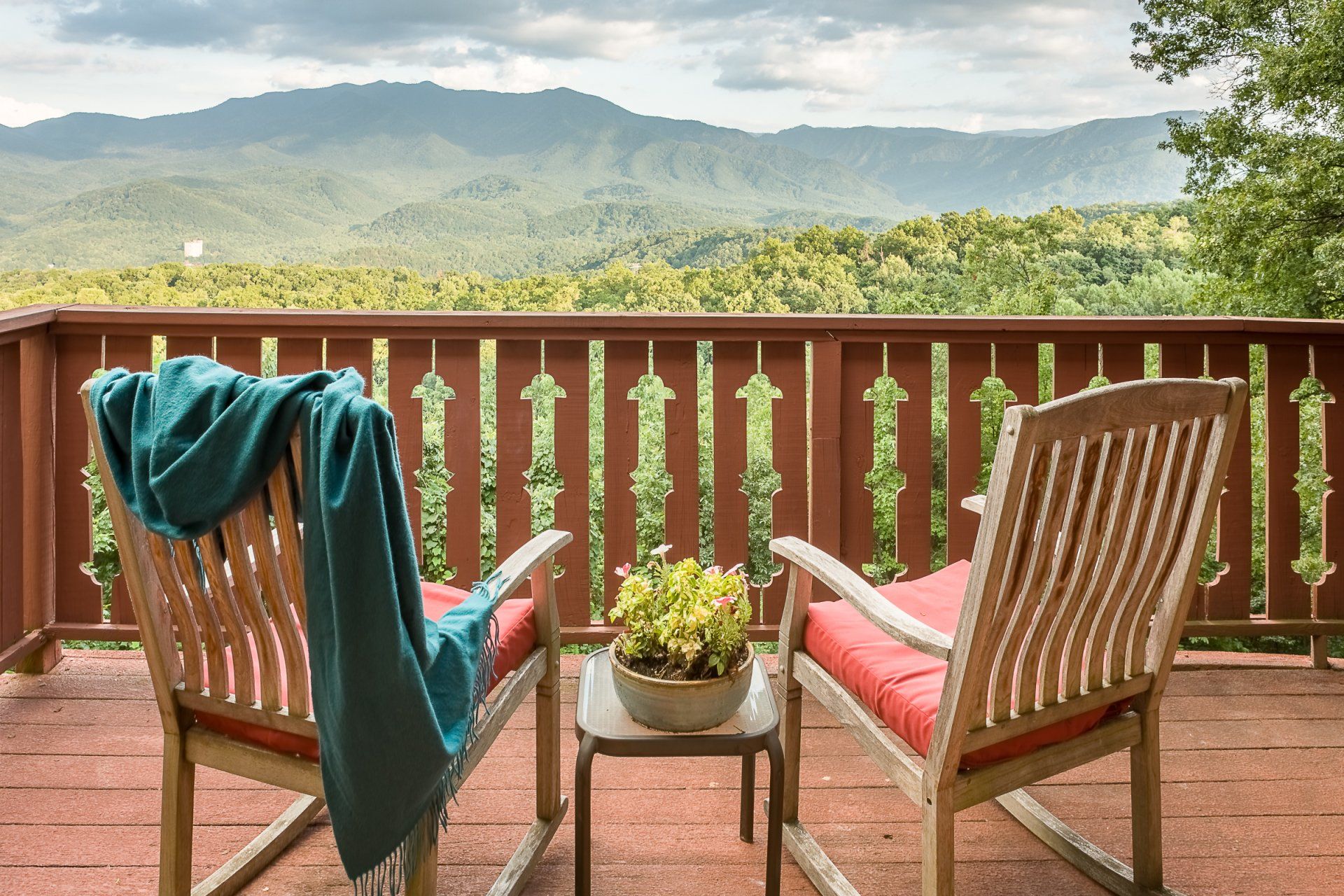 Two rocking chairs and a table on a deck with mountains in the background.