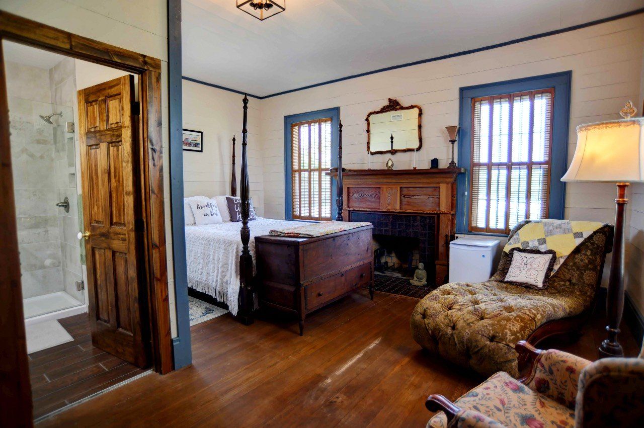 A bedroom with a bed , chair , fireplace and mirror.