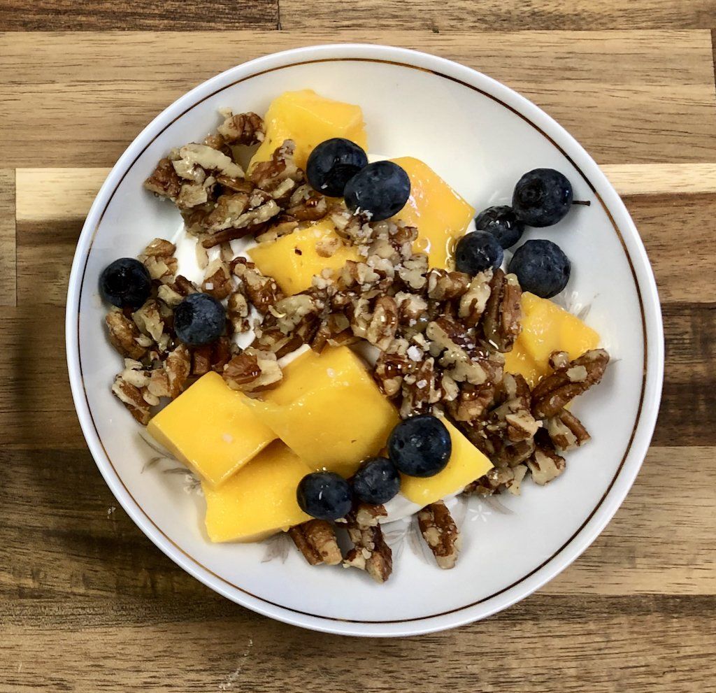 A white plate topped with fruit and nuts on a wooden table