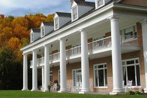 A large house with a porch and chairs in front of it.