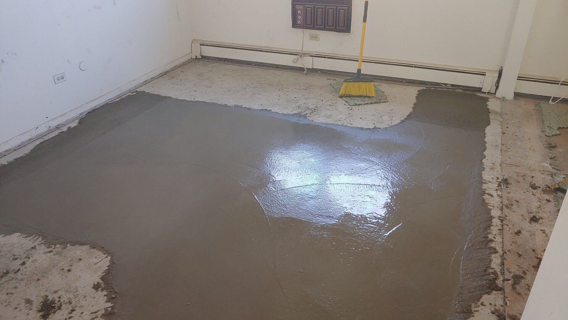 Room with fresh concrete floor being smoothed with a broom.