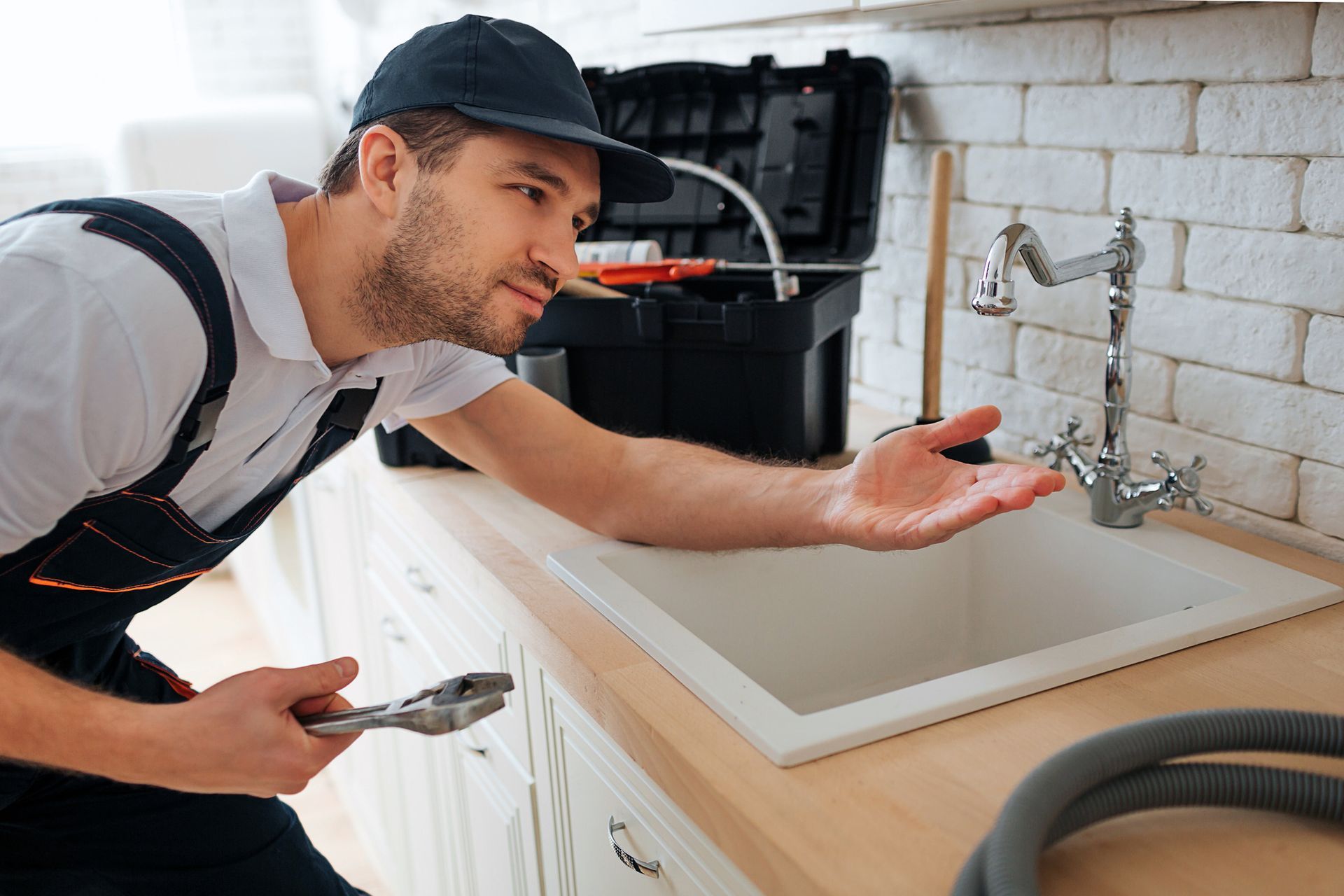 Plumber inspecting kitchen sink faucet with toolbox, checking for leaks and plumbing issues.