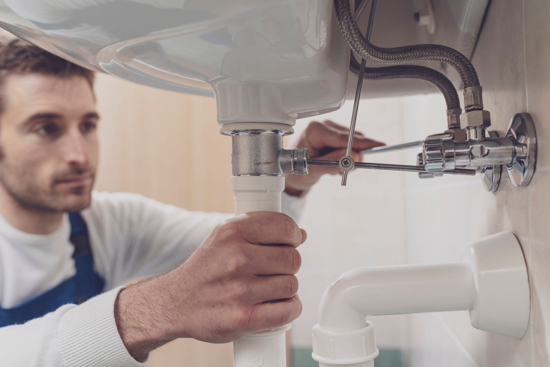 A male plumber is fixing the sink pipe with a wrench. A male plumber is fixing the sink pipe with a wrench.