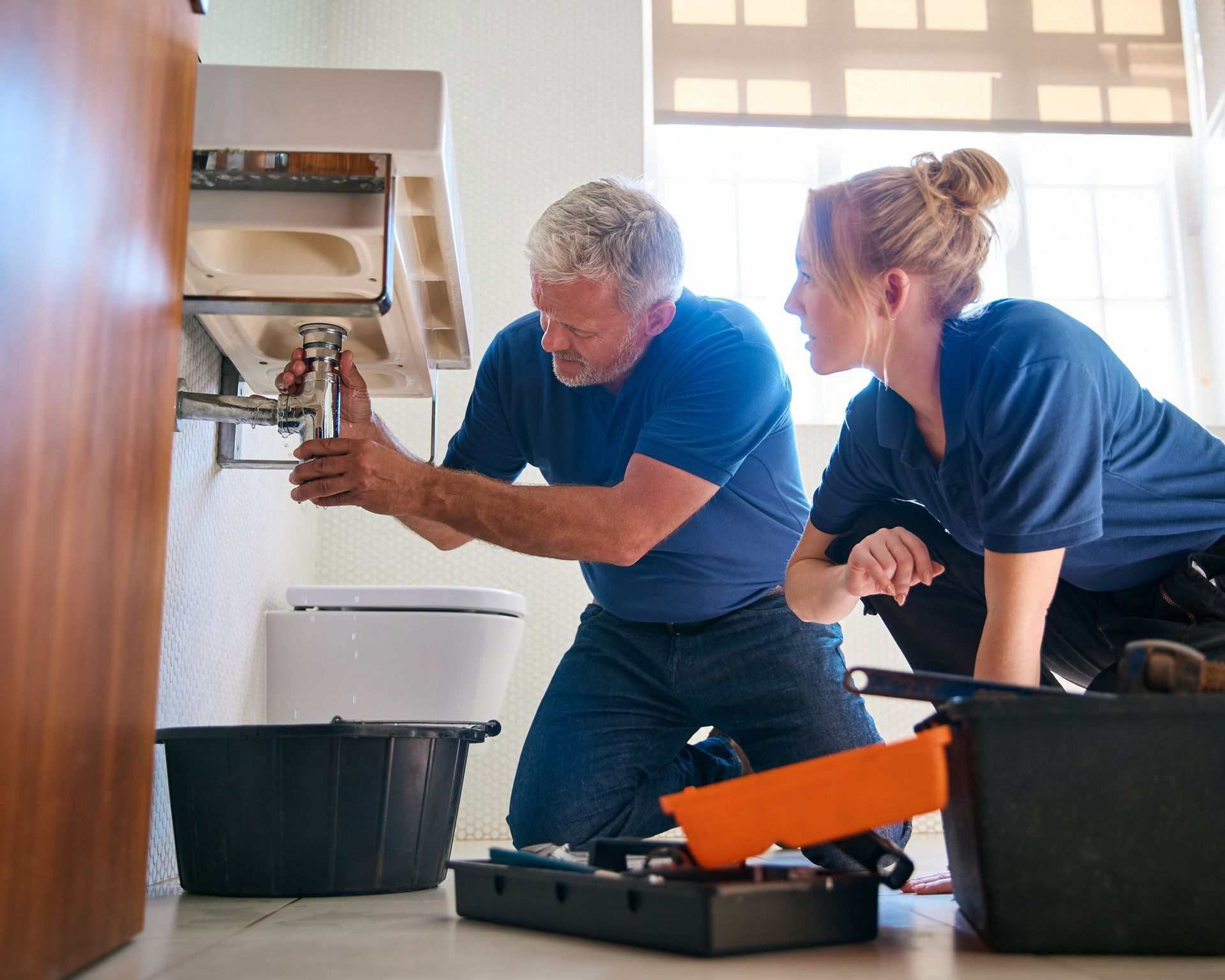 Two emergency plumbing contractors are fixing a leak in a bathroom sink