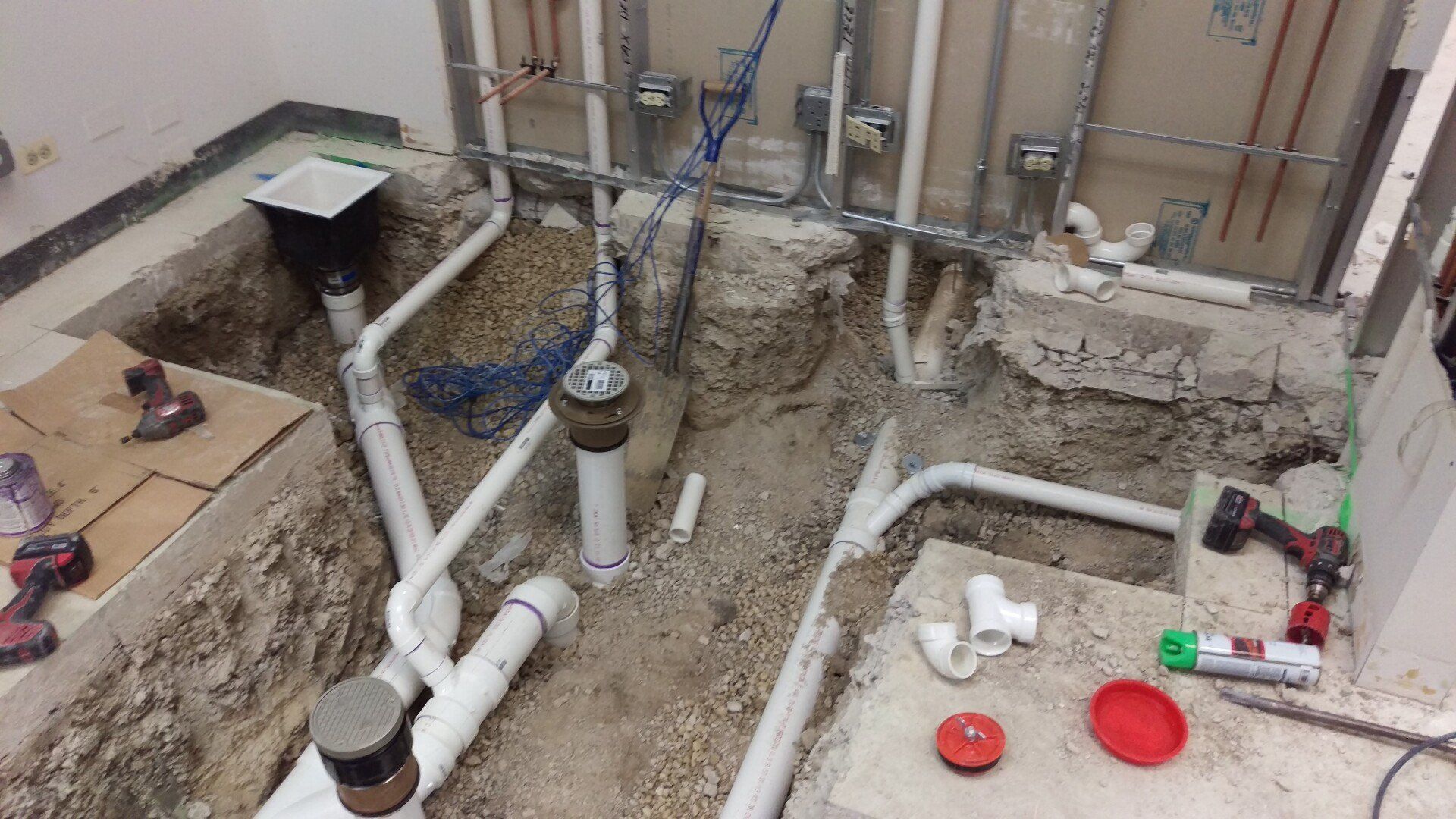 Plumbing renovation: pipes and fittings exposed in a dug-out area, tools and materials nearby.