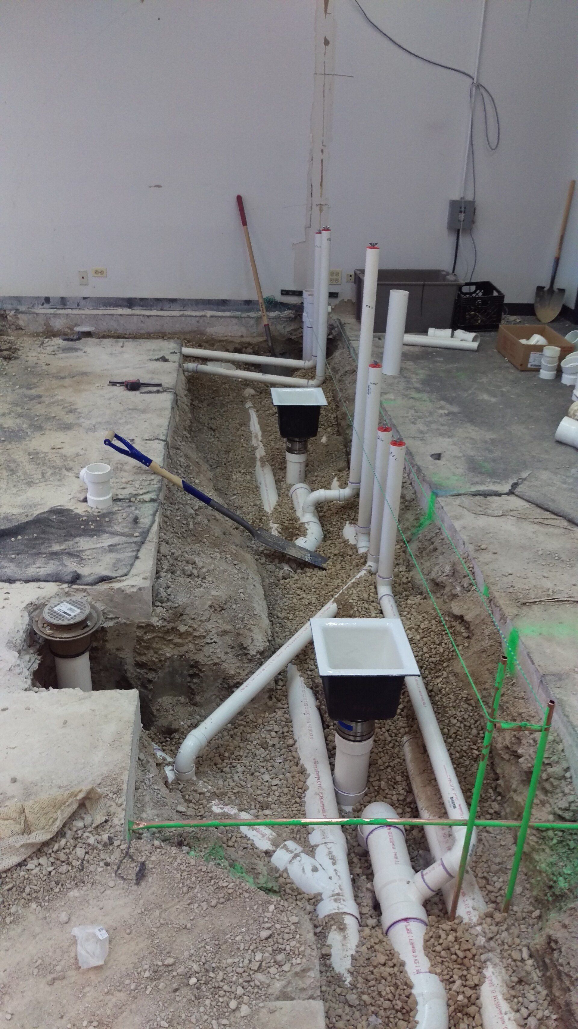 Construction site with exposed plumbing in a trench; white pipes and drains.