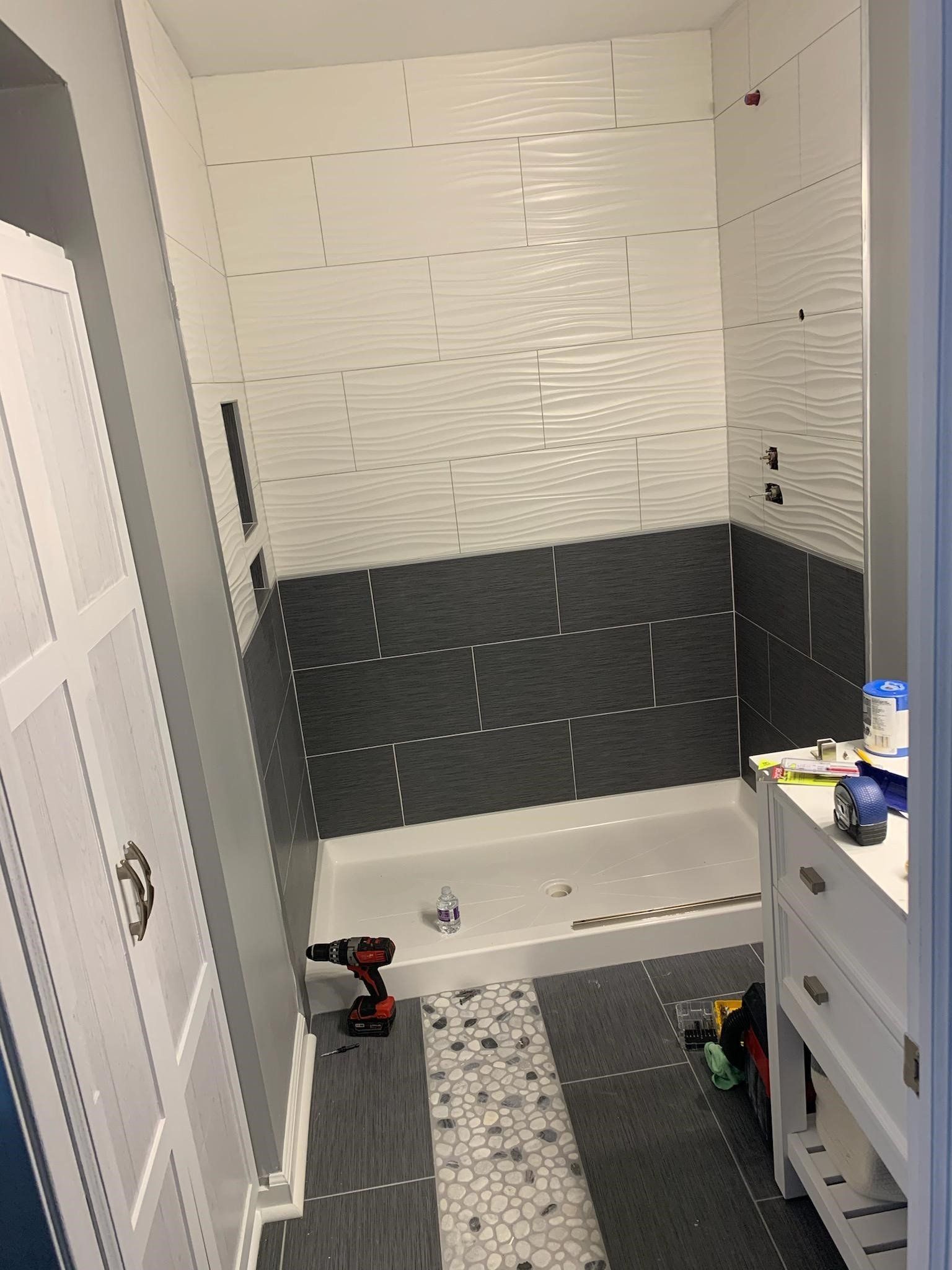 Bathroom with gray and white tiled walls, white vanity, and tiled floor under construction.
