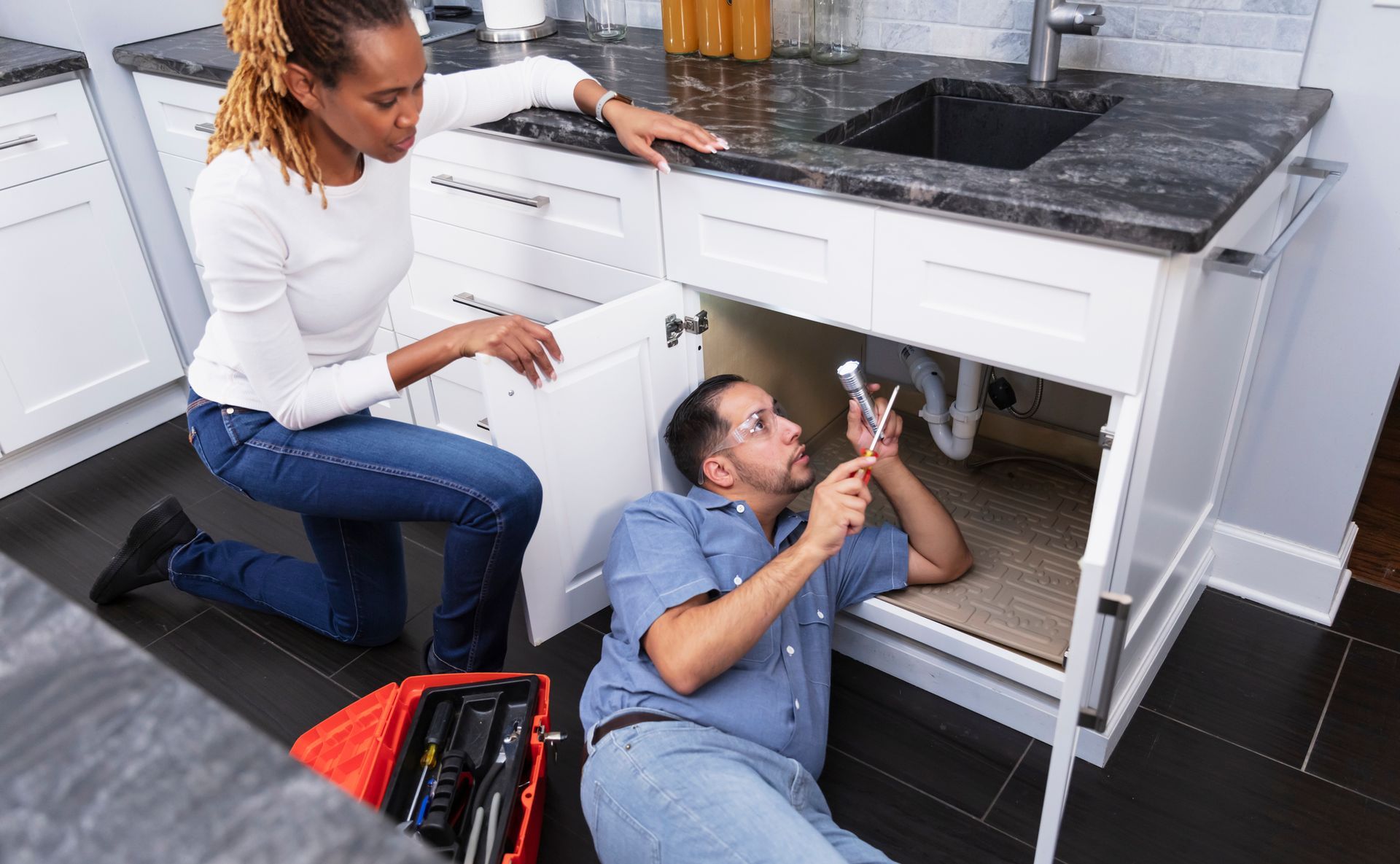 Emergency plumbing contractor using a flashlight to look for a leak under the kitchen sink