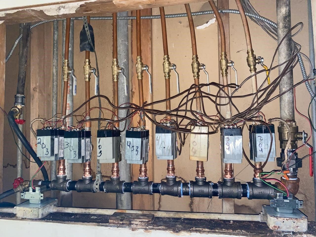 Plumbing manifold system with copper pipes and multiple valves in a wall cavity.