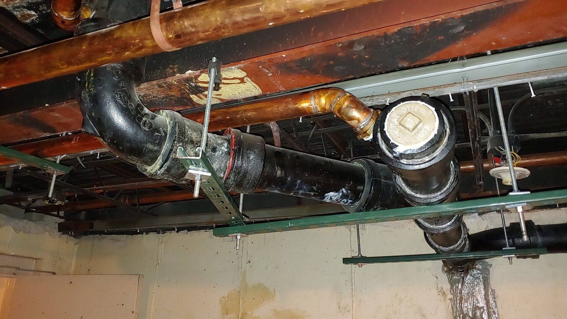 Black plumbing pipes and copper pipes under a ceiling in a building.