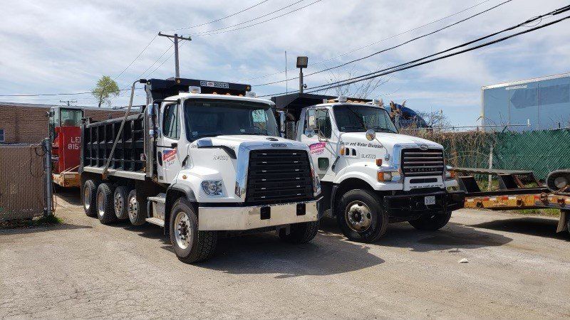 Two white dump trucks parked in a lot under a blue sky.