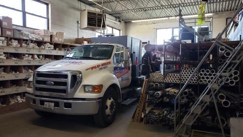White work truck parked inside a warehouse, surrounded by shelves and equipment.