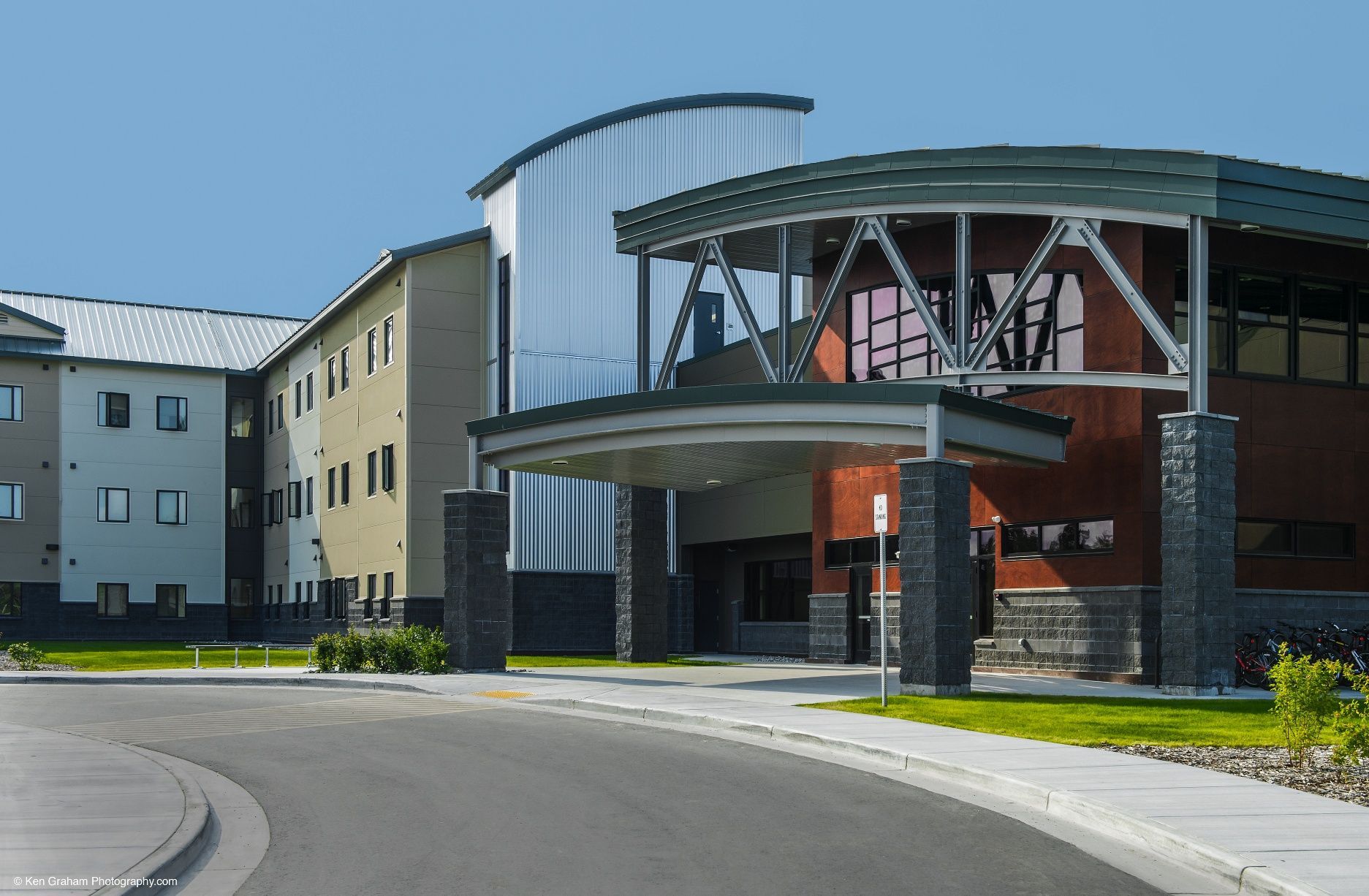 Building with curved metal roof, stone columns at entrance, and a gray asphalt driveway.