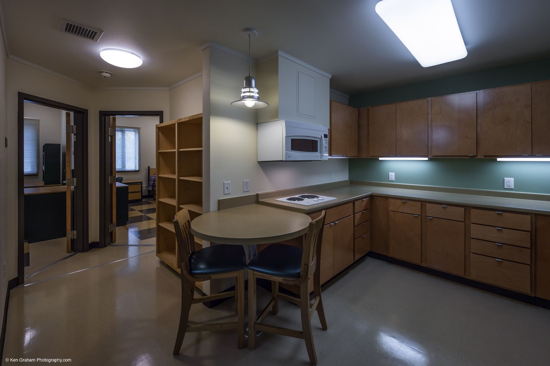 Kitchen with light wood cabinets, a round table, and doorways leading to other rooms.