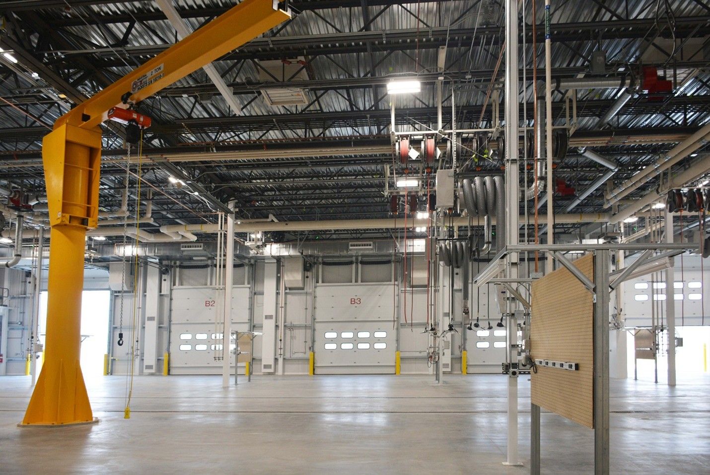 Interior of a large industrial warehouse; a yellow jib crane, garage doors, and metal structures are visible.