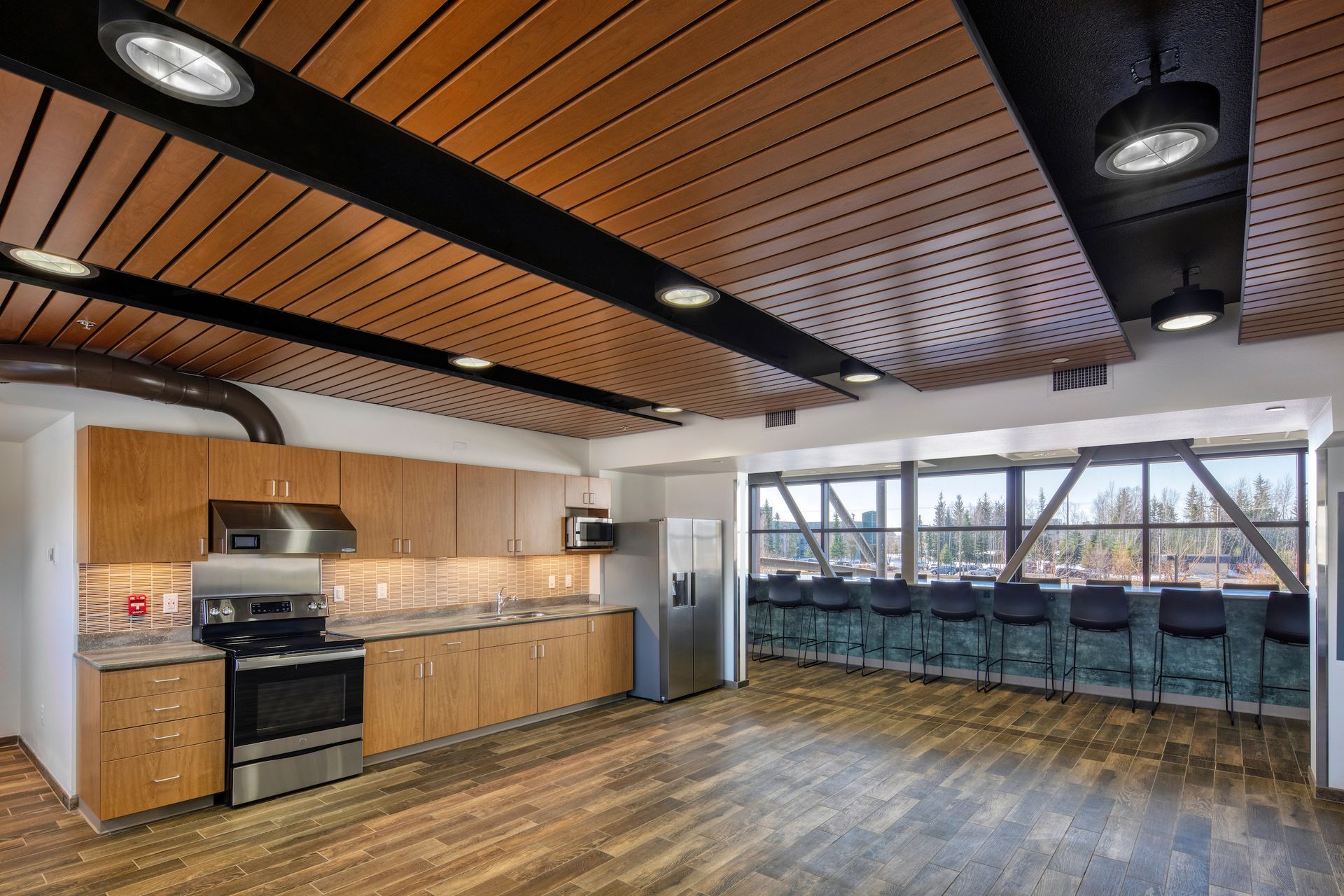 Kitchen with wood ceiling, cabinets, appliances, and a row of chairs along a window.