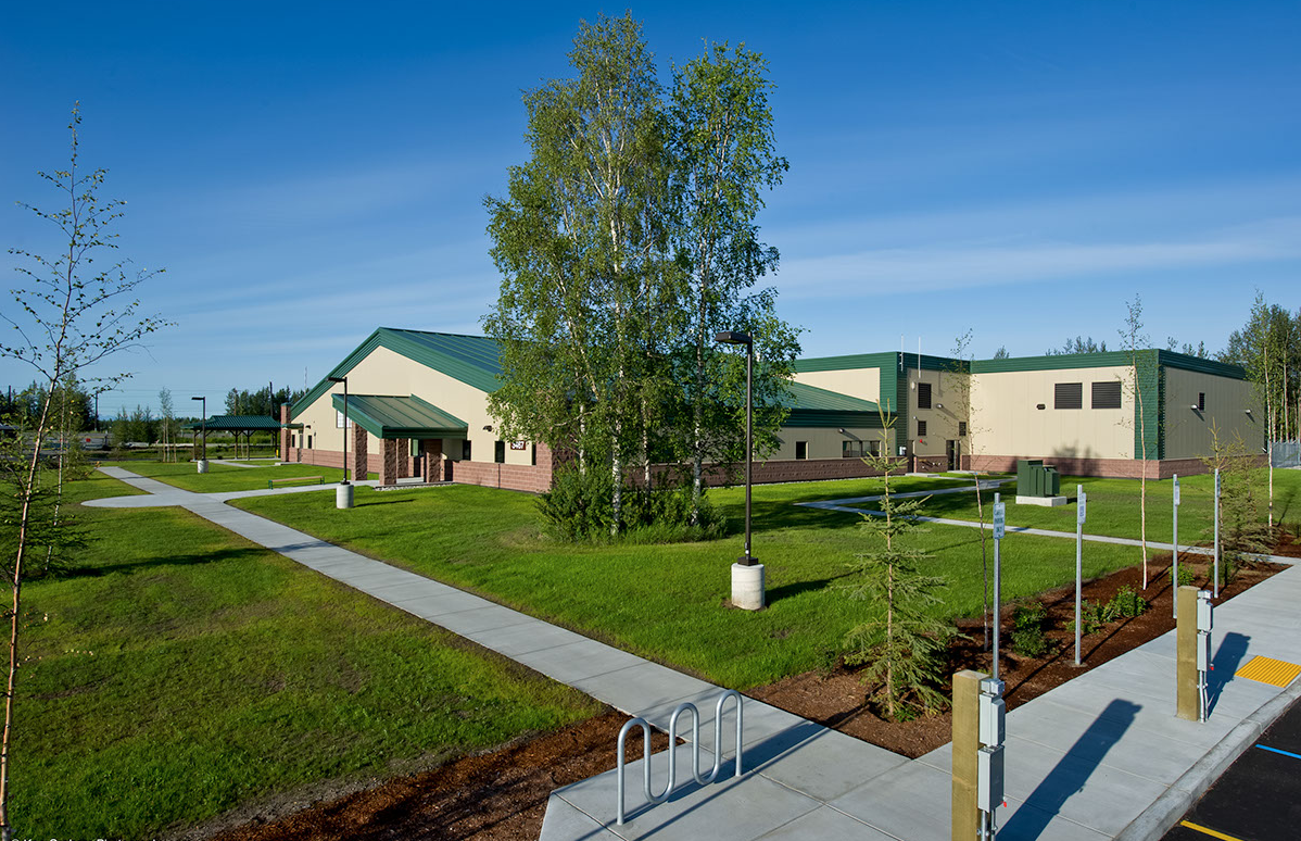 Beige building with green roof and grass lawn under a blue sky.