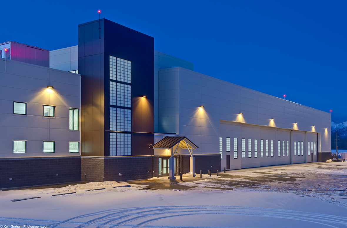 A modern, illuminated airport hangar with a dark blue night sky in the background.
