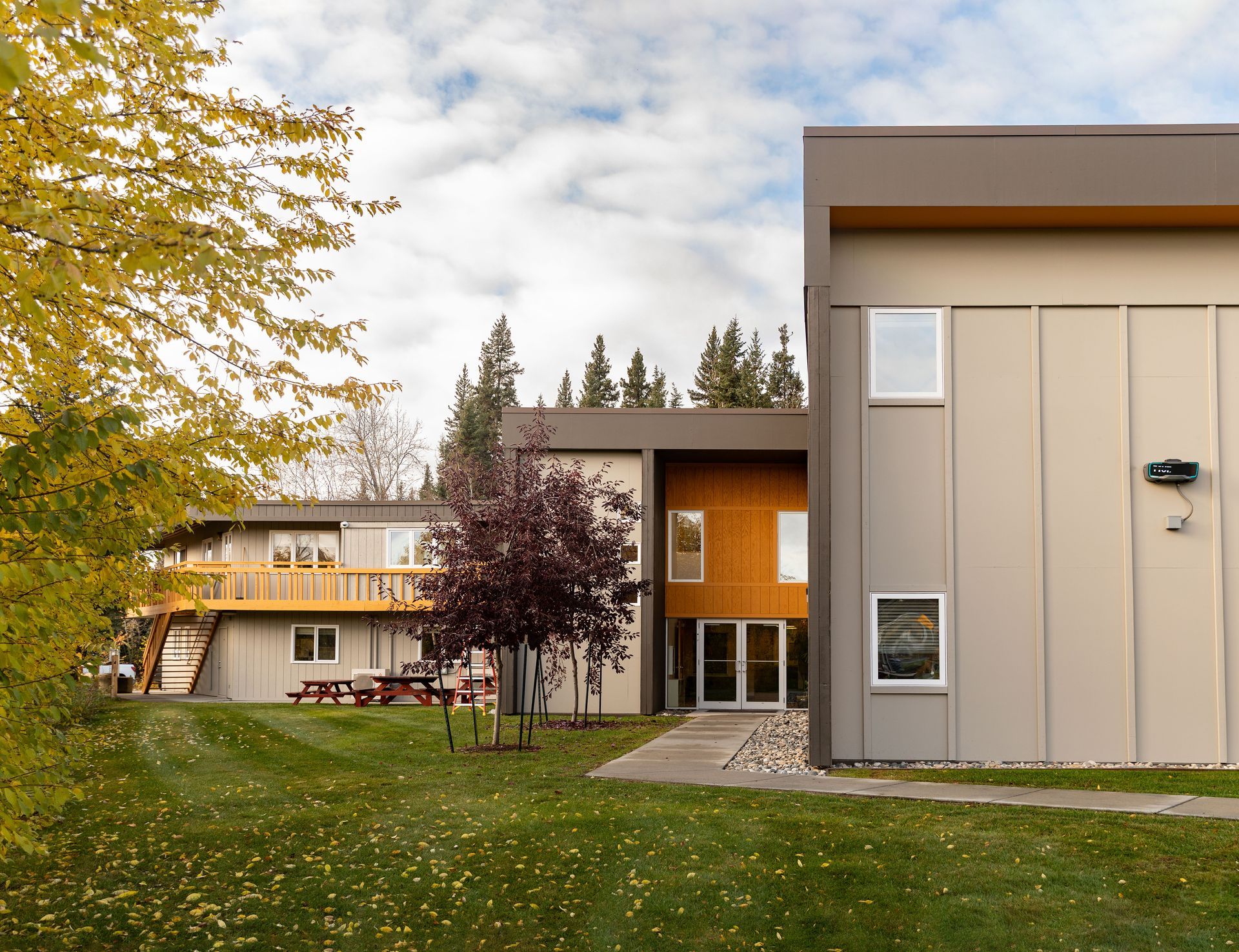 Beige and brown building with lawn and trees, blue sky.