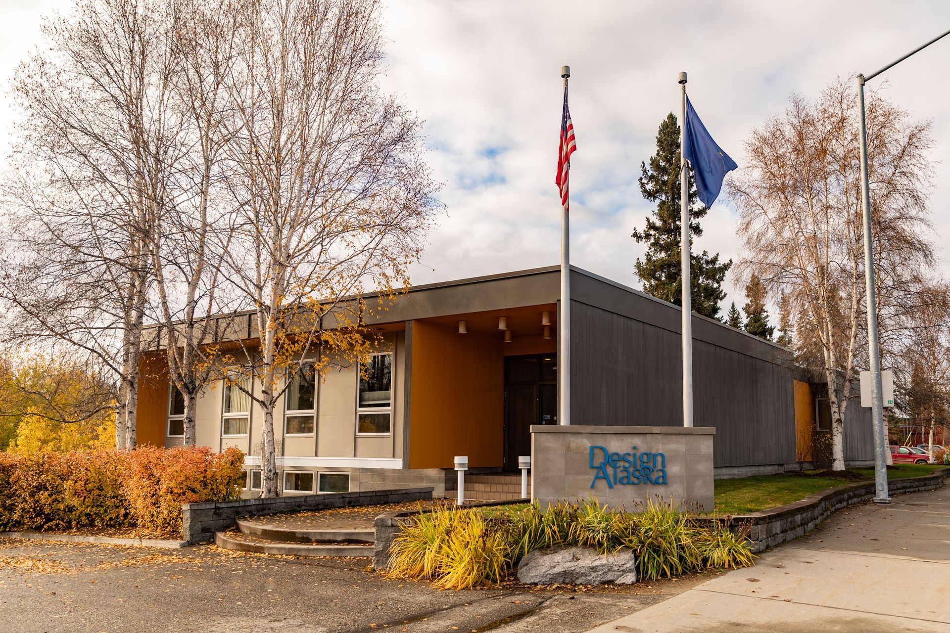 Building with two flags, one red and one blue, trees, and autumn foliage.