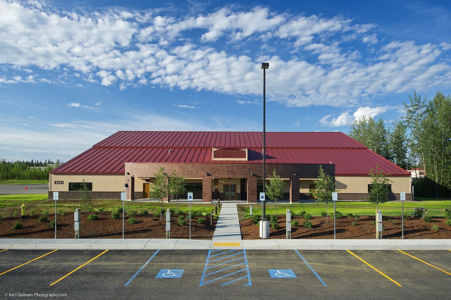 Building with red roof and brown facade. Accessible parking in front. Blue sky with clouds.