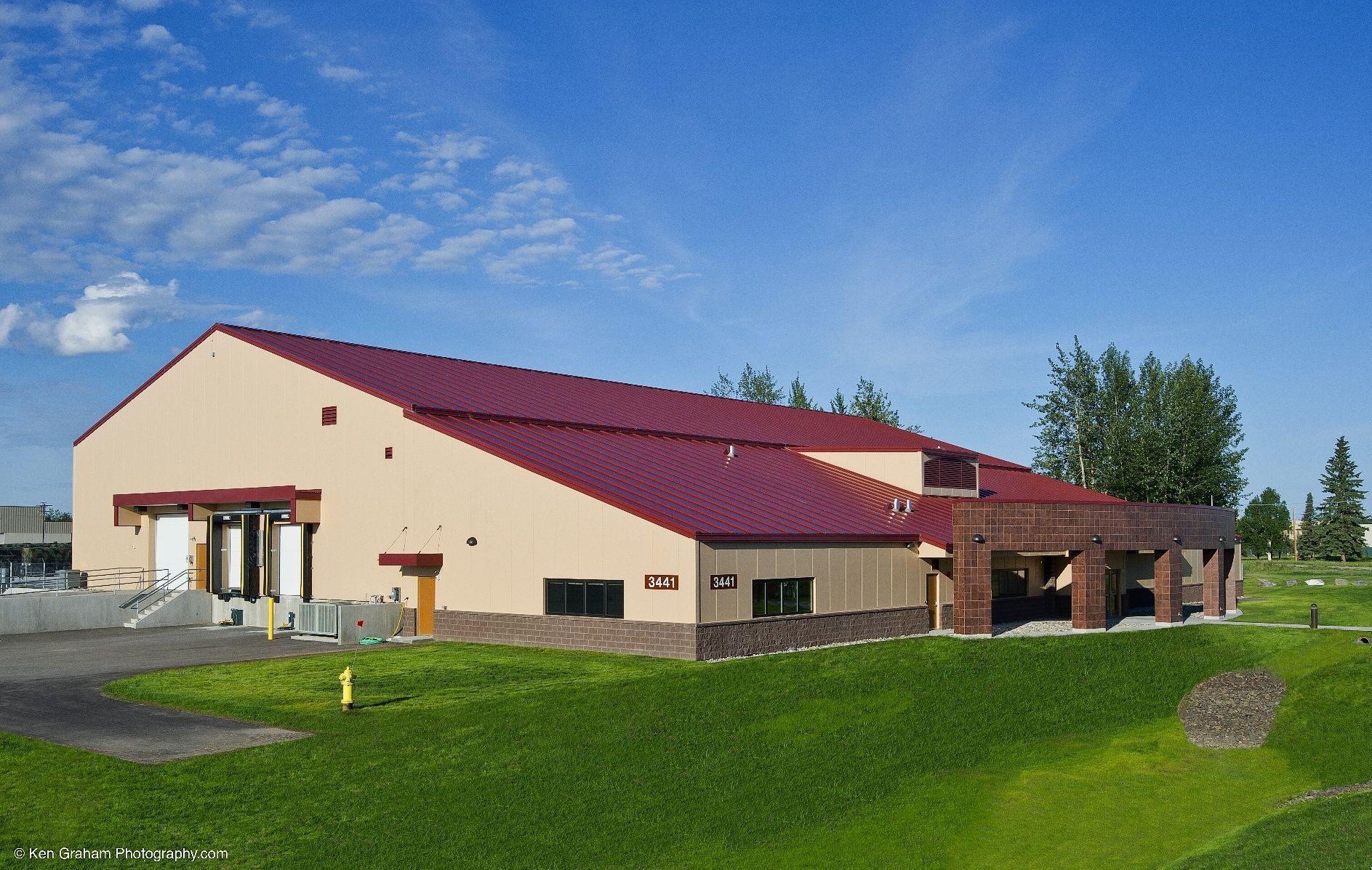 Tan building with burgundy roof and brick accents on green lawn, blue sky.