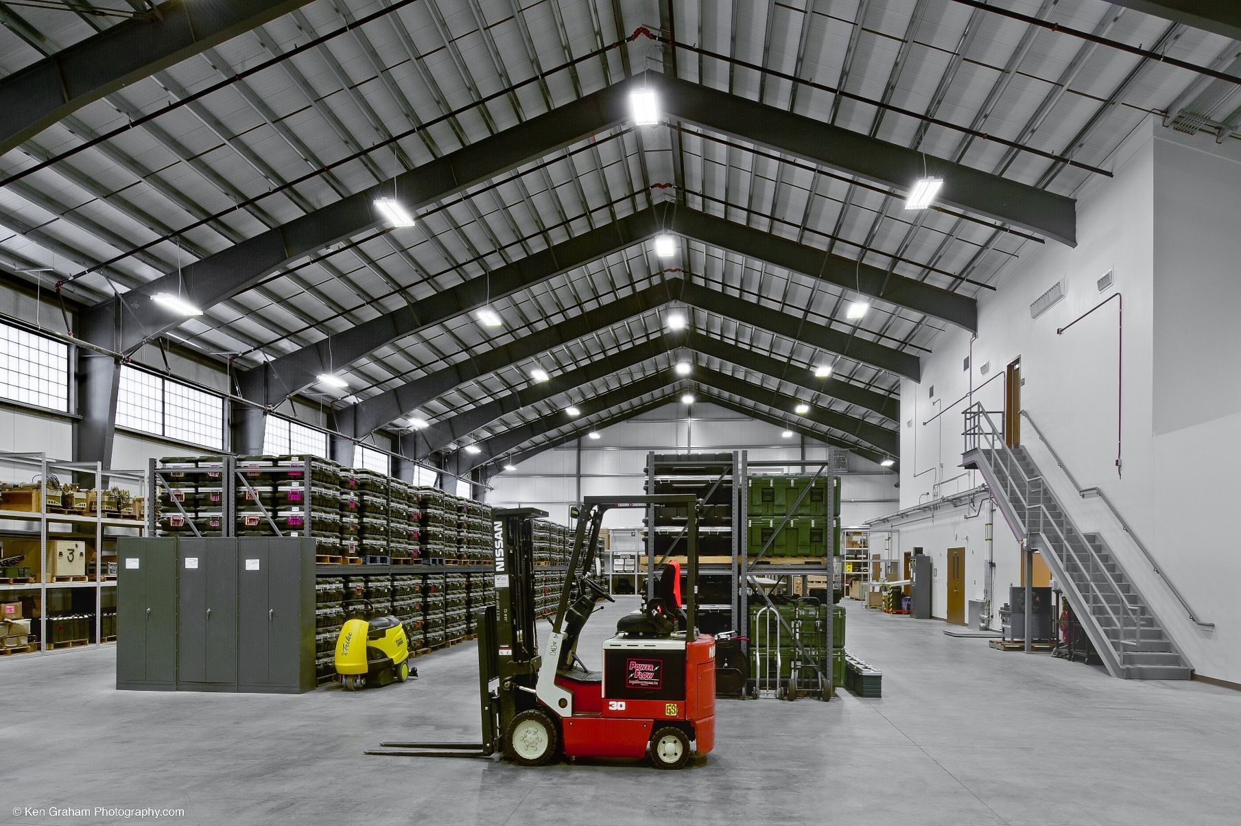 Red forklift in a large warehouse with metal roof and shelves.