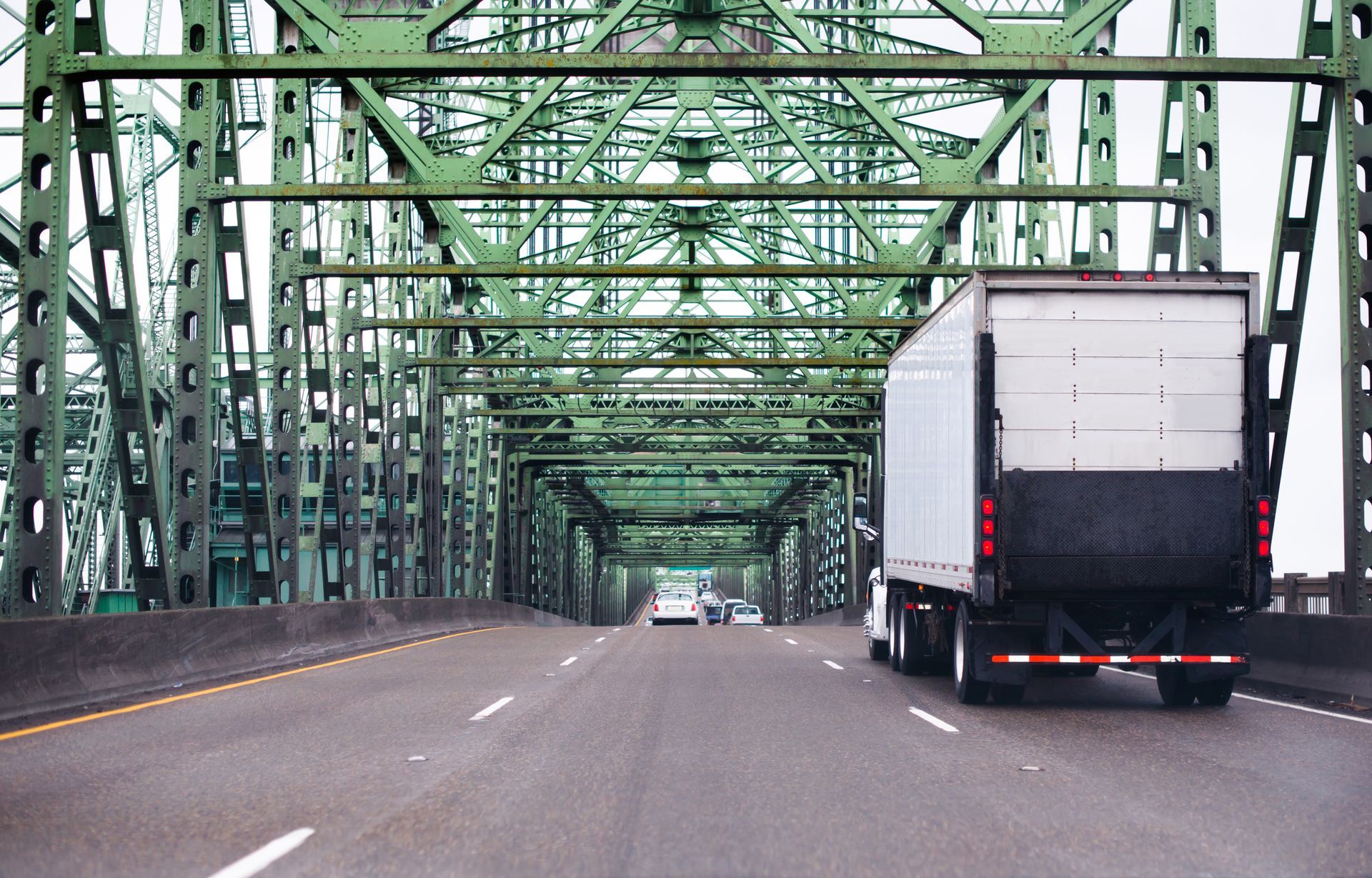 A white truck is driving on a highway under a bridge.