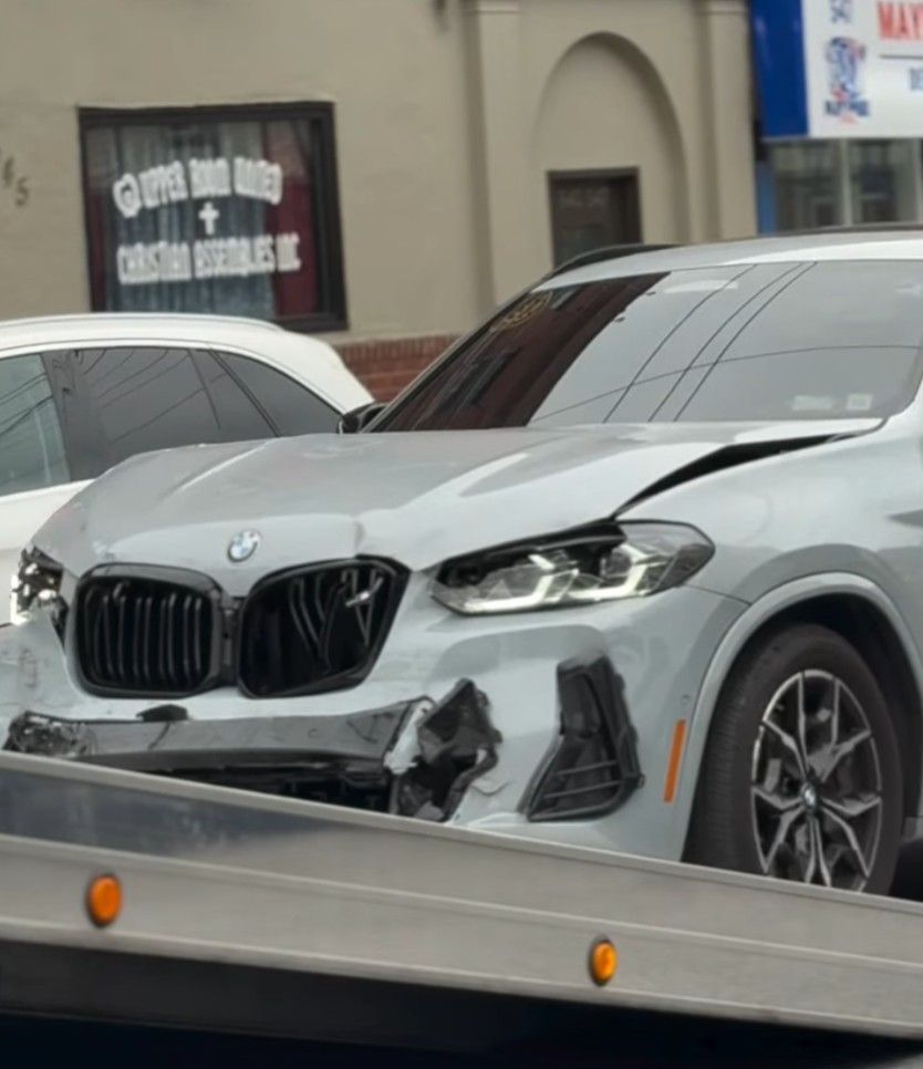 A gray car that was in an accident is being rolled of of a tow truck in front of an auto body shop in Mount Vernon, NY.
