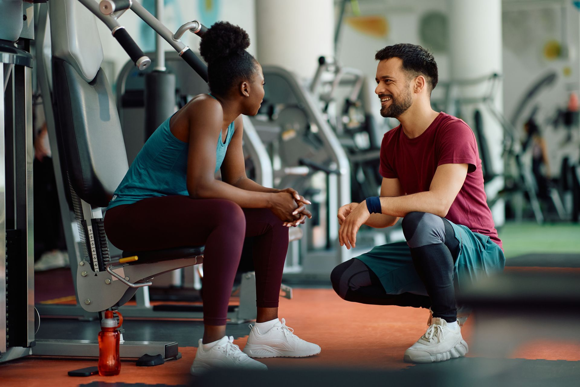 A man and a woman are sitting on a bench in a gym talking to each other.
