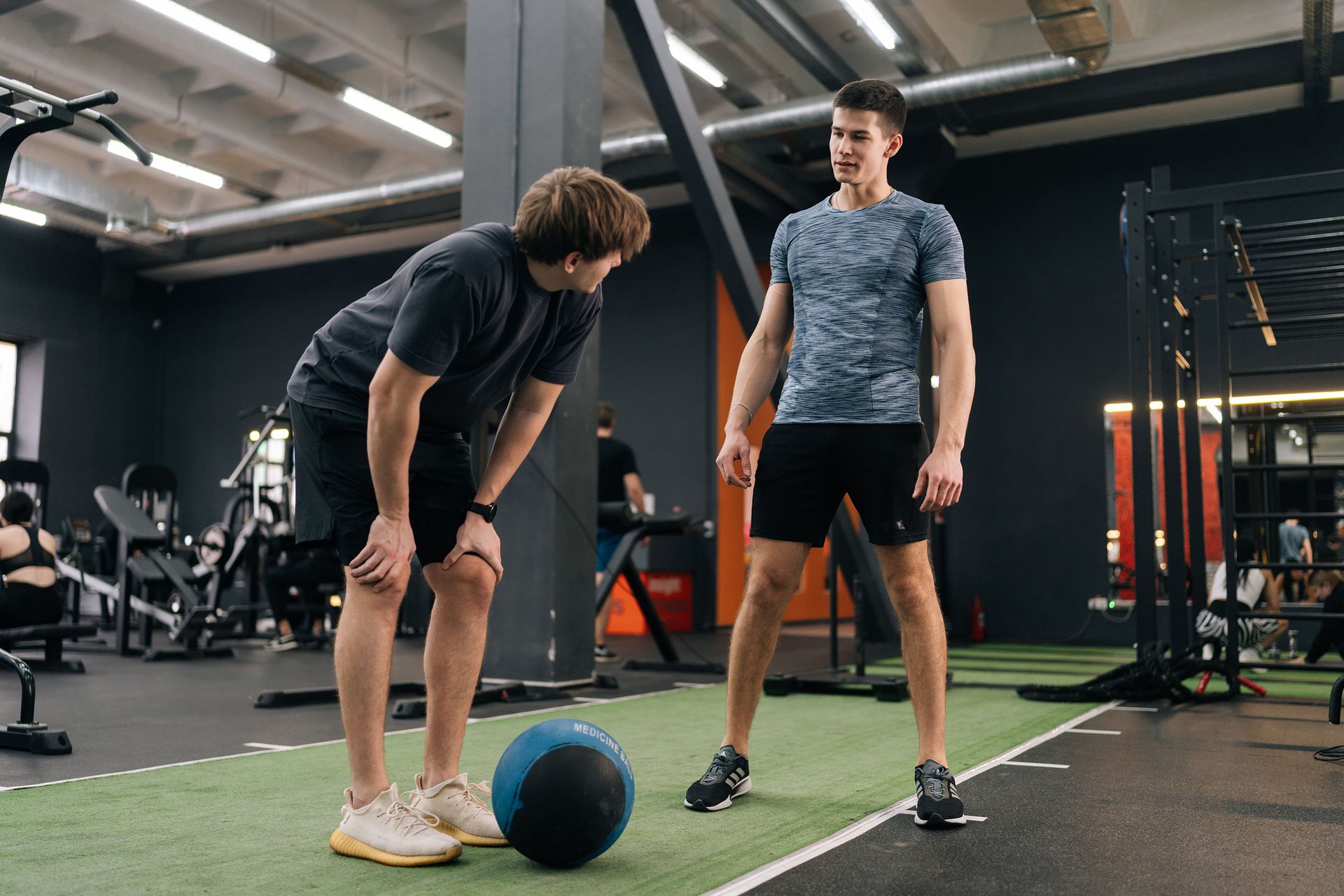 Two men are standing next to a medicine ball in a gym.