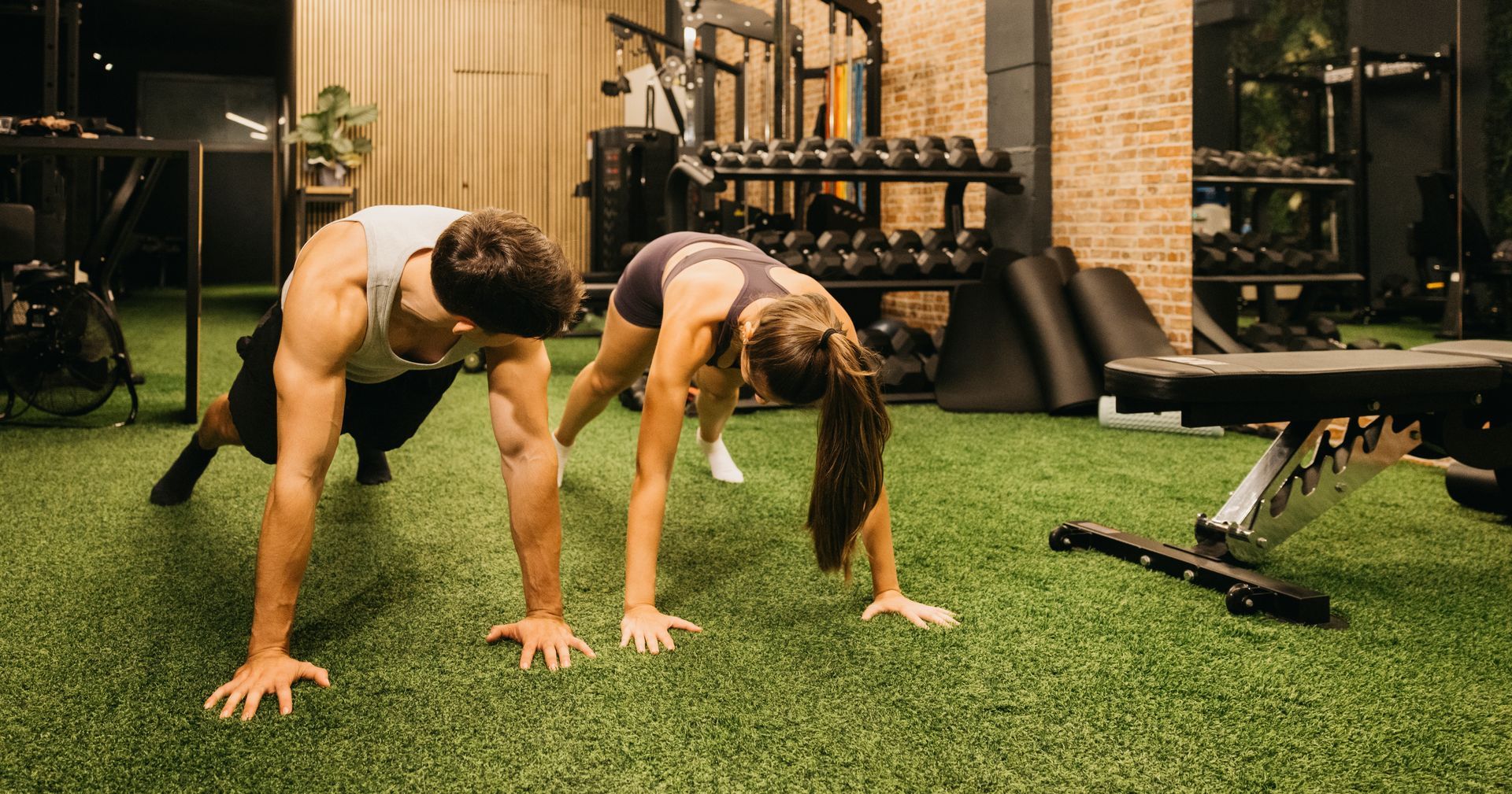 Two people doing a workout in a gym. They are in a push-up position with their legs bent.