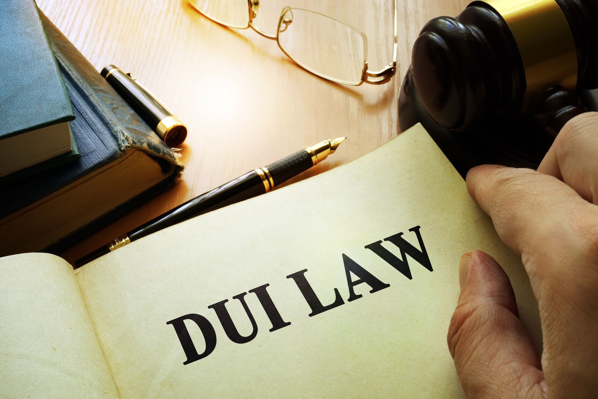 Open book titled 'DUI Law' on a desk with glasses, a pen, and a gavel nearby.
