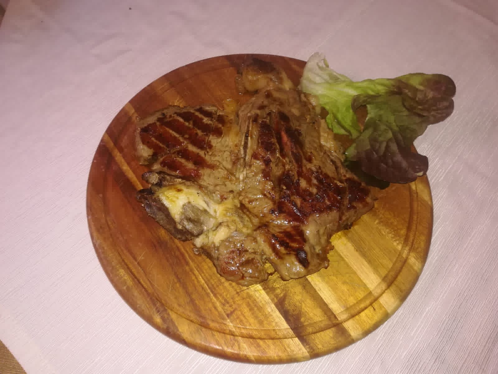 Bistecca alla griglia su un piatto di legno con i segni della grigliatura, servita con un piccolo contorno di lattuga.