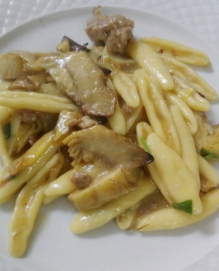 Piatto di pasta con carciofi e carne, su un piatto bianco.