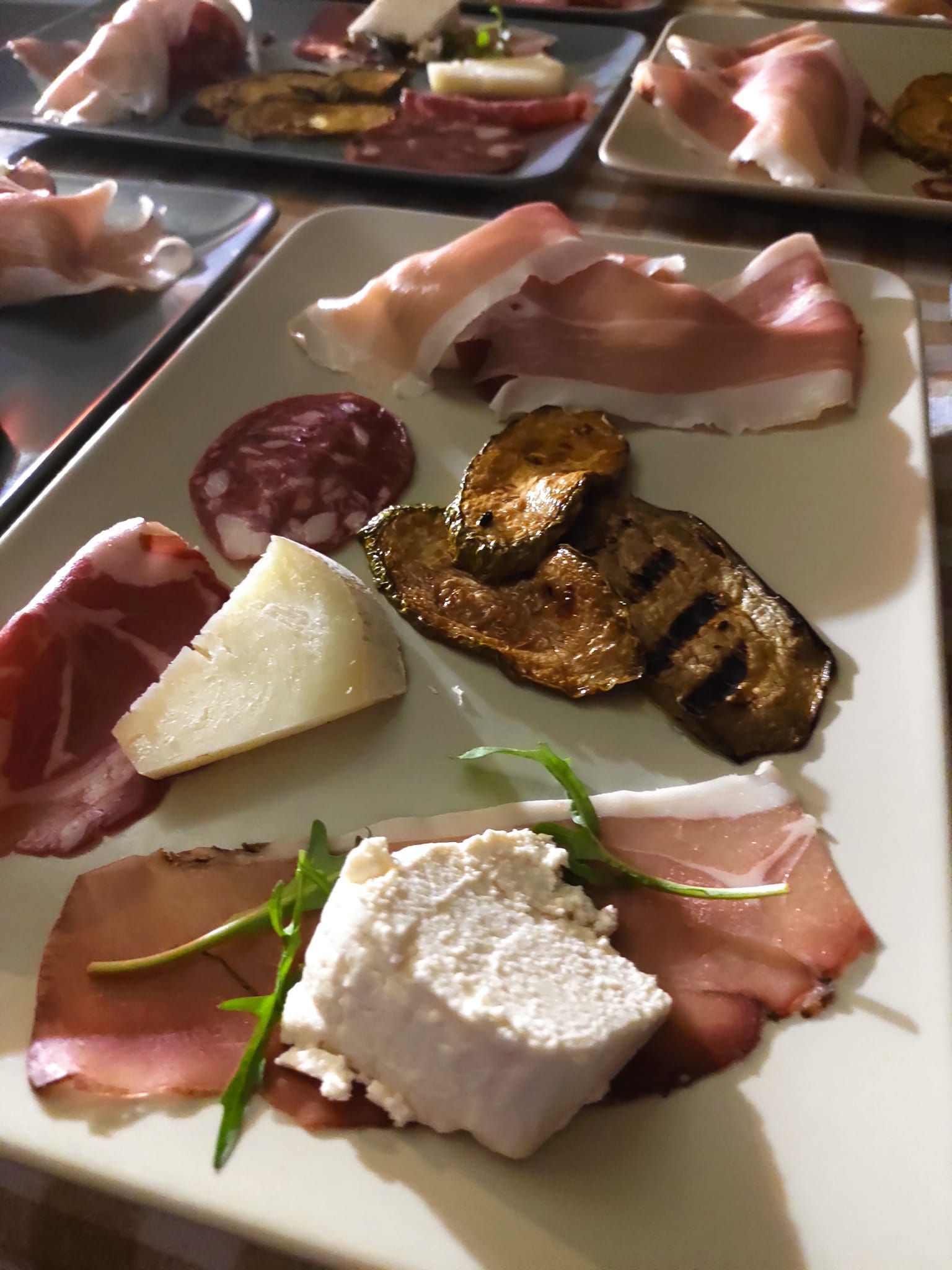 Tagliere di salumi con carni assortite, formaggi e verdure grigliate su un piatto rettangolare.