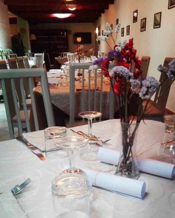 Tavolo del ristorante apparecchiato con bicchieri, posate e bouquet di fiori, con altri tavoli sullo sfondo.