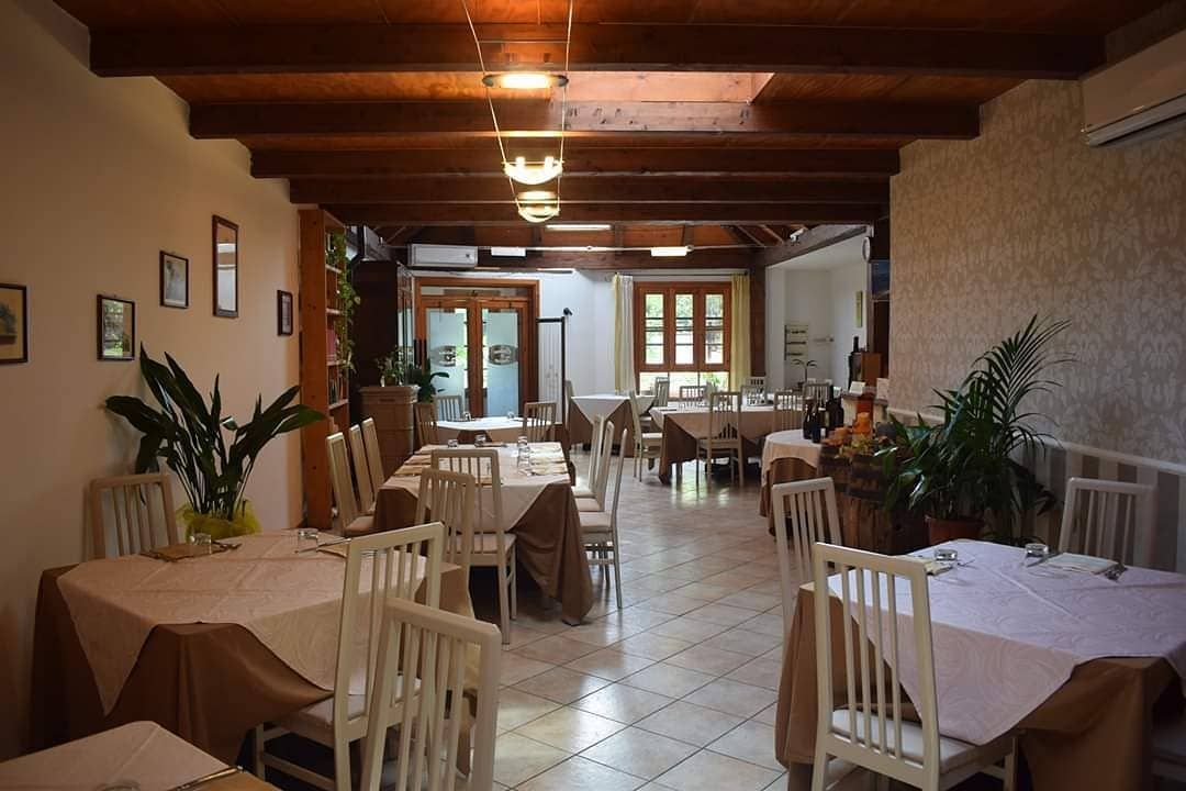 Interno del ristorante: tavoli bianchi, sedie, tovaglie color cuoio chiaro, travi in ​​legno scuro, piante.