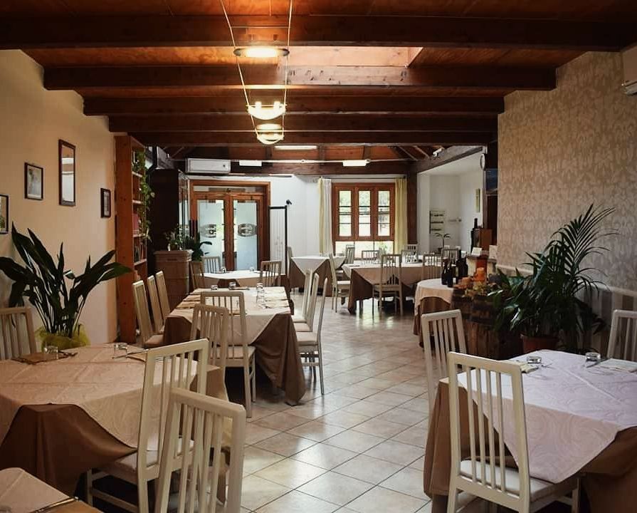 Interno vuoto di un ristorante con sedie bianche, tovaglie beige e soffitto in legno.