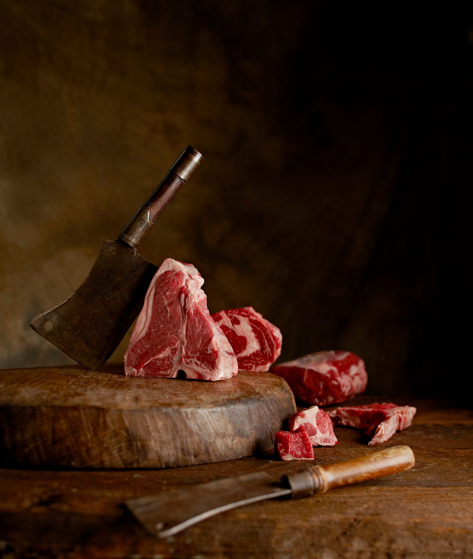 Tagliare la carne su un tagliere di legno con una mannaia, in un ambiente scarsamente illuminato.