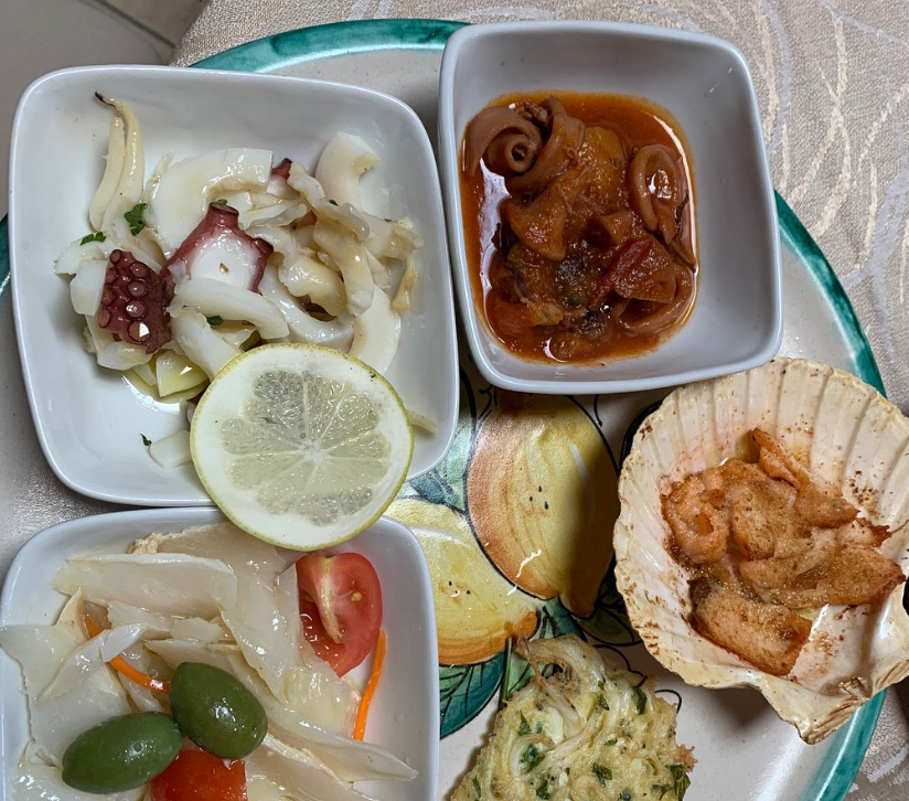 Piatto di antipasti di mare: polpo, calamari, gamberi, verdure marinate, fetta di limone e olive.