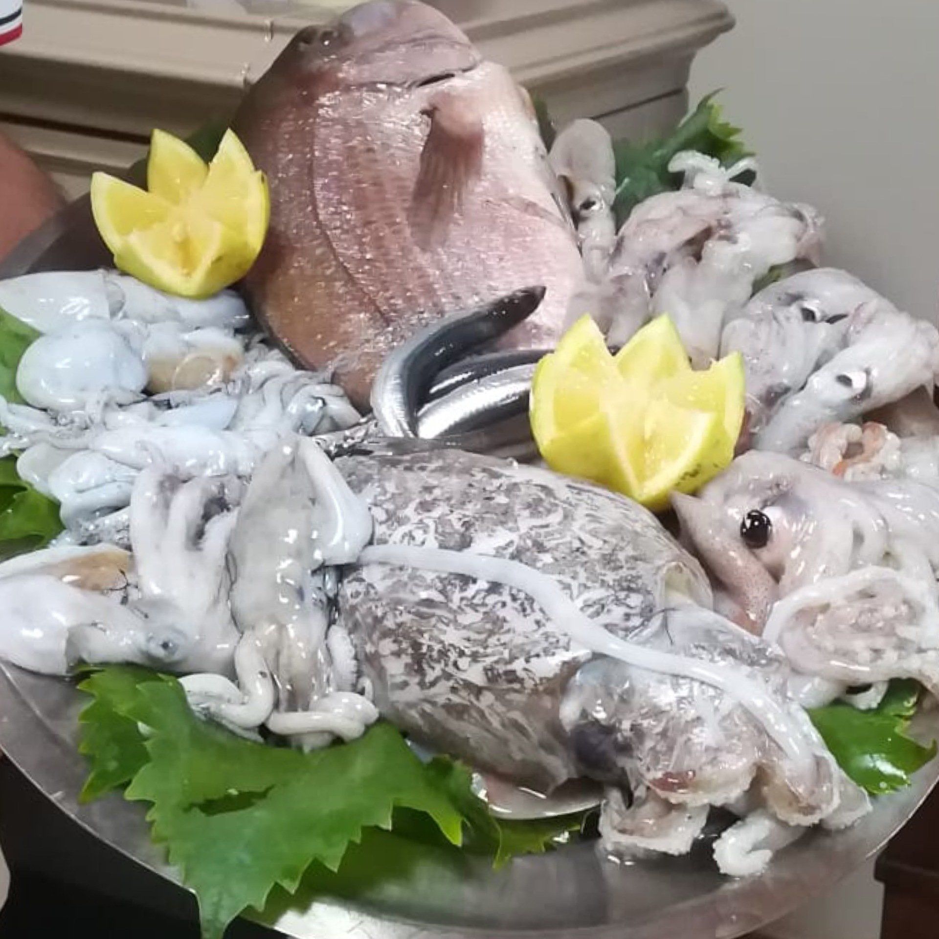 Piatto di frutti di mare con pesce, calamari e polpo, guarnito con fette di limone e verdure.